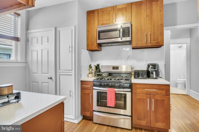 kitchen with appliances with stainless steel finishes, light hardwood / wood-style flooring, light stone counters, and tasteful backsplash