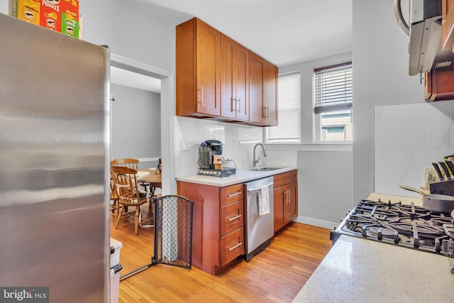 kitchen featuring sink, light hardwood / wood-style flooring, light stone counters, and stainless steel appliances