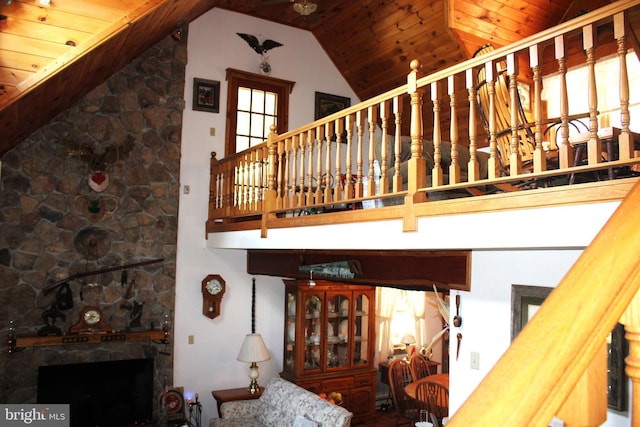 stairway featuring a stone fireplace, high vaulted ceiling, and wood ceiling