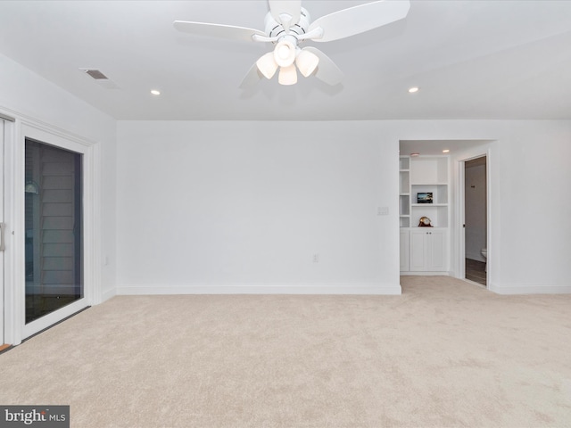 unfurnished room with built in shelves, light colored carpet, and ceiling fan