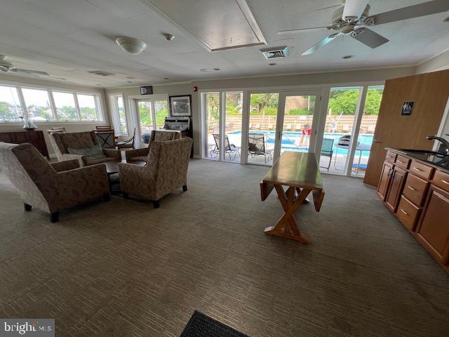 living room with ceiling fan, sink, carpet floors, and ornamental molding