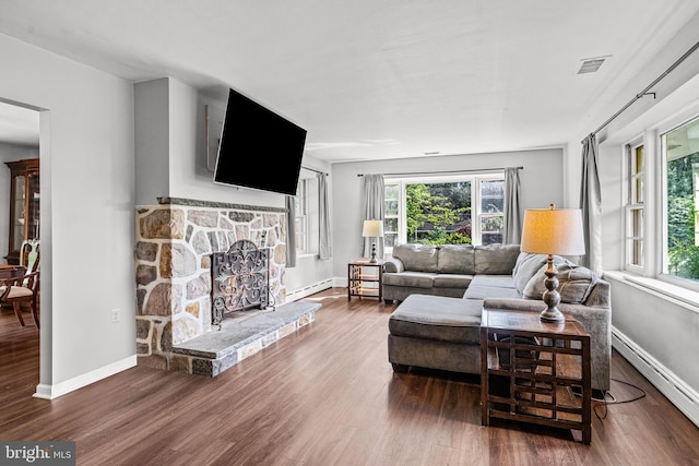 living room with a stone fireplace, dark hardwood / wood-style flooring, and a baseboard radiator