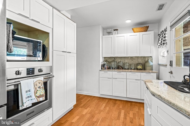 kitchen with white cabinetry, light stone counters, light hardwood / wood-style floors, decorative backsplash, and appliances with stainless steel finishes