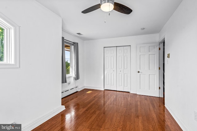 unfurnished bedroom with ceiling fan, dark wood-type flooring, baseboard heating, and a closet