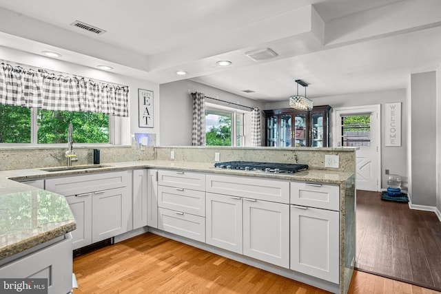 kitchen featuring white cabinets, stainless steel gas stovetop, sink, and decorative light fixtures