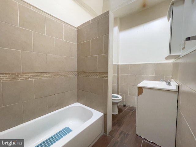 full bathroom featuring tiled shower / bath, vanity, toilet, and tile walls