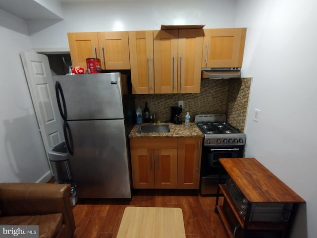 kitchen featuring backsplash, extractor fan, black gas range, light stone countertops, and stainless steel fridge