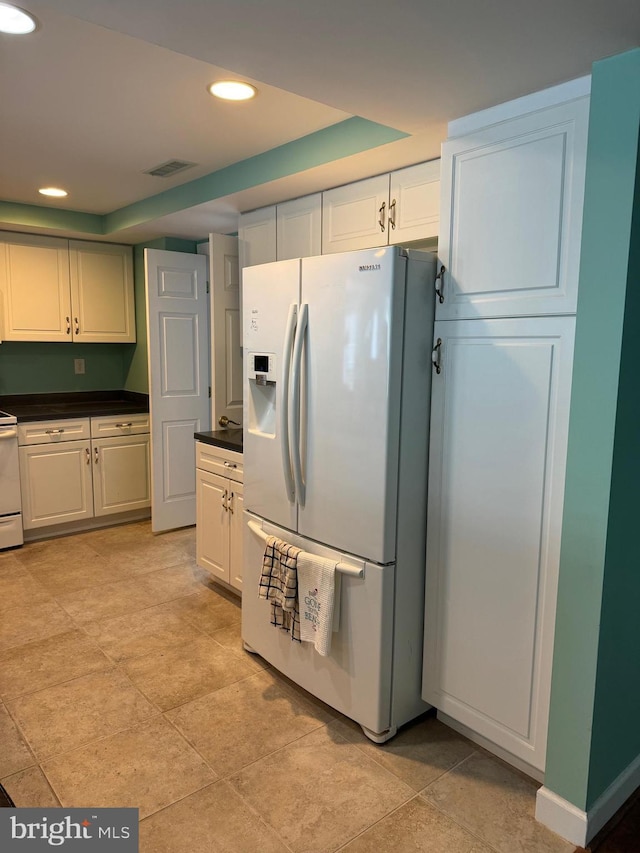 kitchen with a raised ceiling, white cabinets, white fridge with ice dispenser, and range