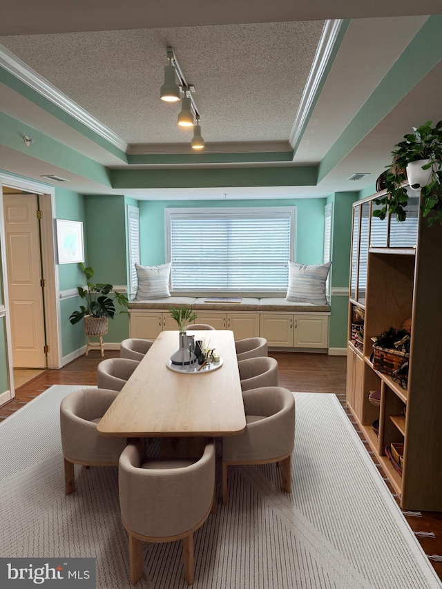 dining area with hardwood / wood-style flooring, ornamental molding, a textured ceiling, and a raised ceiling