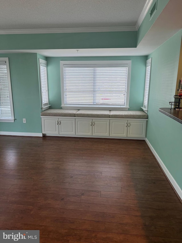 empty room with dark wood-type flooring, a textured ceiling, and ornamental molding