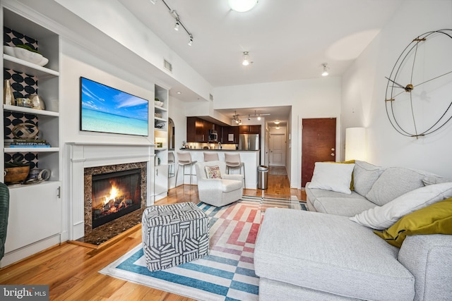 living room featuring a fireplace, track lighting, built in shelves, and light wood-type flooring