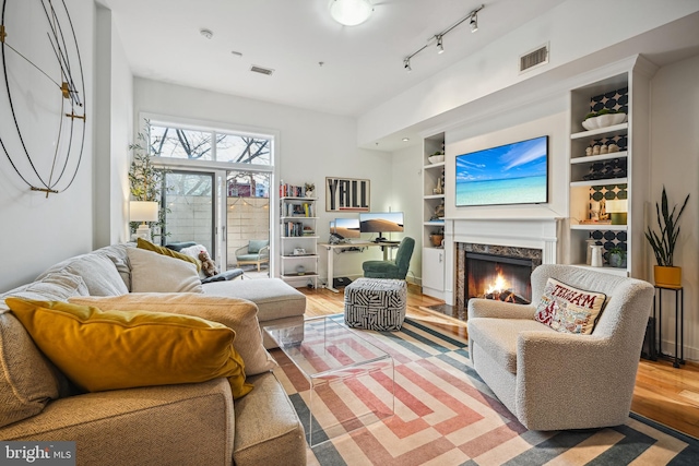 living room with a high end fireplace, rail lighting, built in shelves, and wood-type flooring