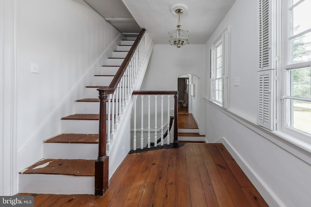 stairs with hardwood / wood-style floors and an inviting chandelier