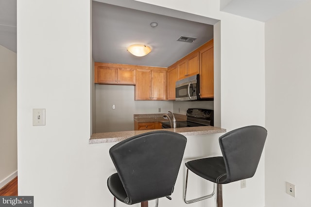 kitchen with electric range, wood-type flooring, kitchen peninsula, and a breakfast bar area