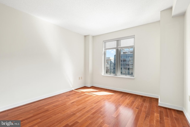 empty room with a textured ceiling and light hardwood / wood-style flooring