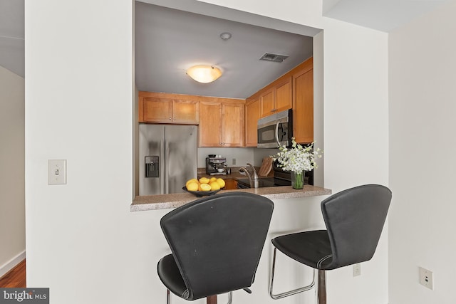 kitchen with a kitchen bar, wood-type flooring, stainless steel appliances, and kitchen peninsula