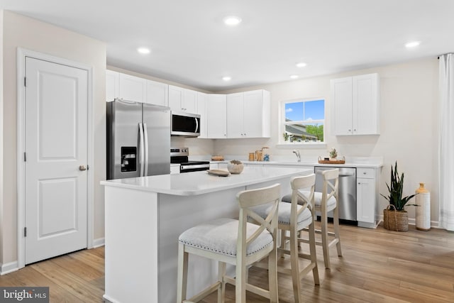 kitchen with a kitchen breakfast bar, light wood-type flooring, appliances with stainless steel finishes, a kitchen island, and white cabinetry