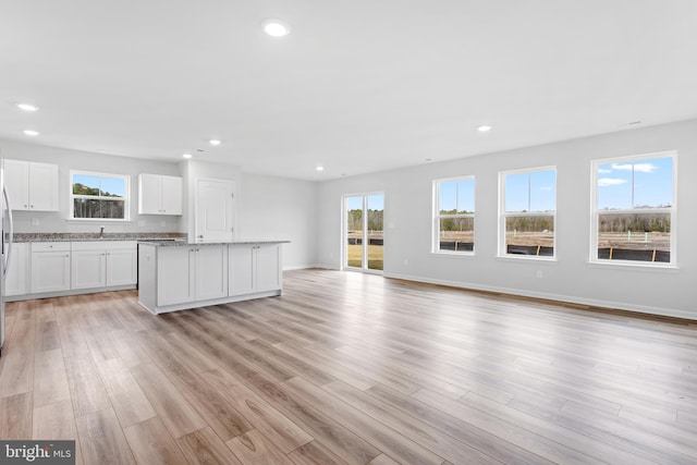 kitchen featuring light hardwood / wood-style flooring, white cabinets, a center island, light stone countertops, and sink