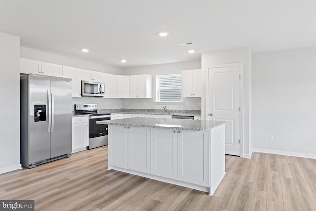 kitchen with white cabinetry, stainless steel appliances, light hardwood / wood-style flooring, and a kitchen island