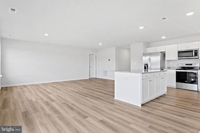 kitchen with light hardwood / wood-style flooring, white cabinets, a kitchen island, light stone countertops, and appliances with stainless steel finishes