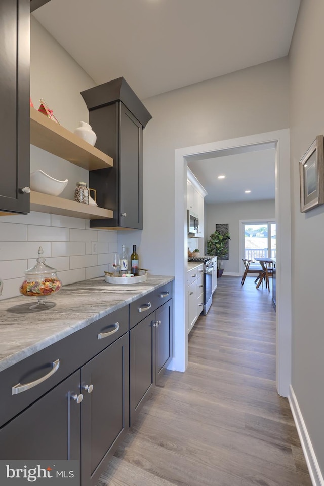 kitchen with tasteful backsplash, light wood-type flooring, light stone countertops, and appliances with stainless steel finishes