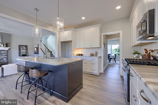 kitchen featuring decorative light fixtures, white cabinetry, a kitchen island with sink, stainless steel appliances, and light stone countertops