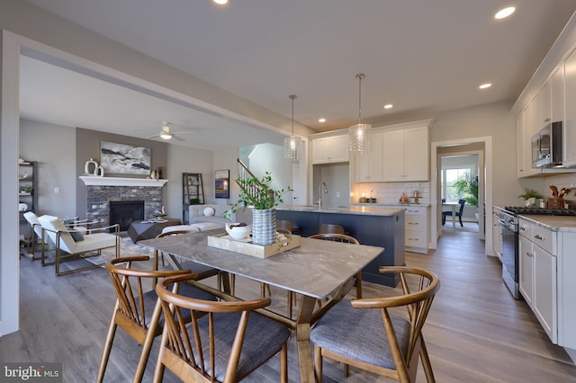 dining area with sink, a fireplace, ceiling fan, and light wood-type flooring