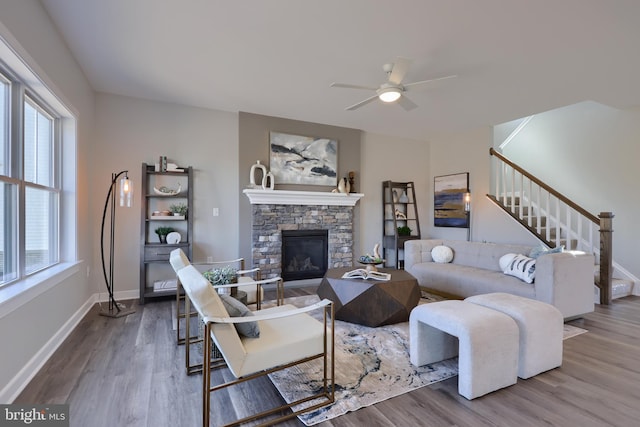 living room with ceiling fan, a stone fireplace, and hardwood / wood-style floors