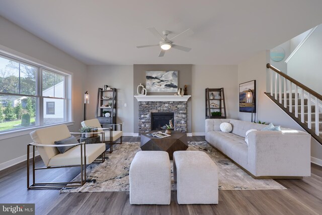 living room with hardwood / wood-style flooring, ceiling fan, and a stone fireplace