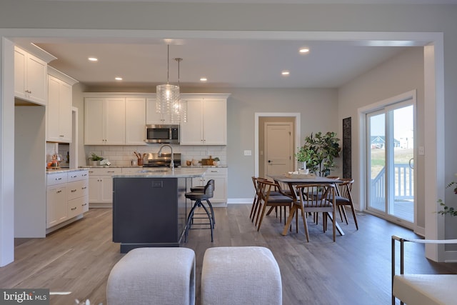 kitchen with decorative light fixtures, an island with sink, white cabinets, and appliances with stainless steel finishes