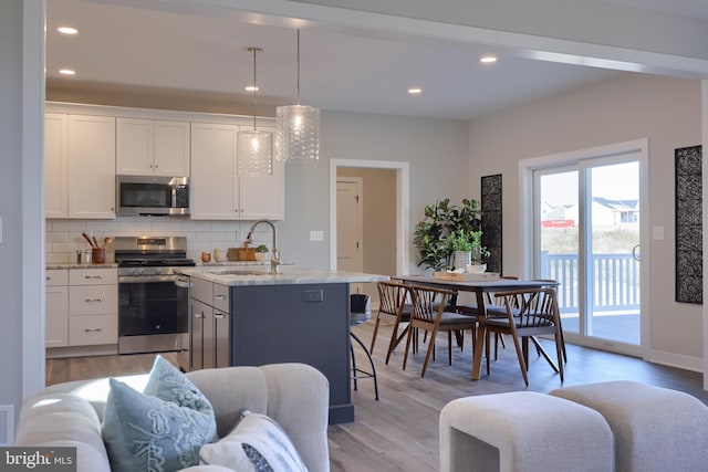 kitchen with pendant lighting, white cabinetry, stainless steel appliances, tasteful backsplash, and an island with sink