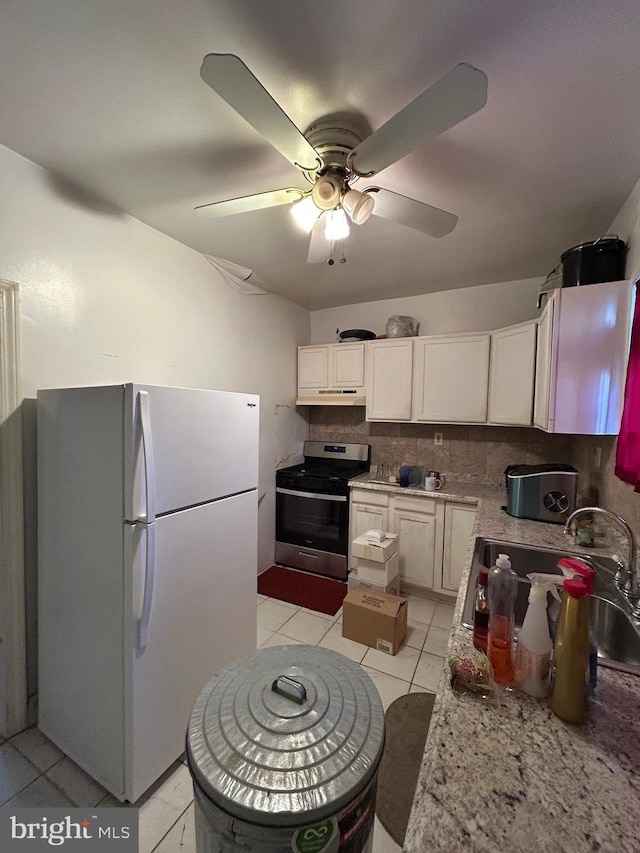 kitchen with white cabinets, backsplash, white fridge, light tile patterned floors, and stainless steel range