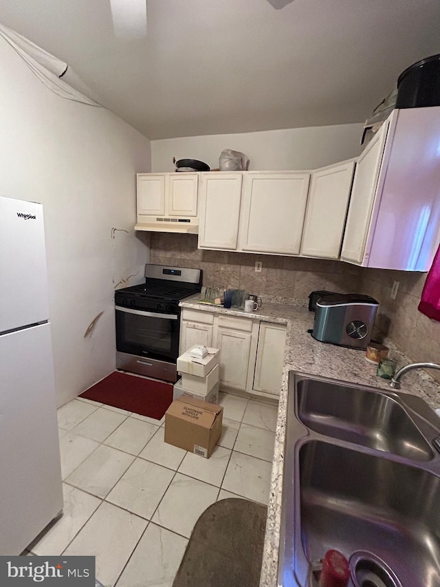 kitchen with refrigerator, sink, backsplash, light tile patterned floors, and stainless steel gas range