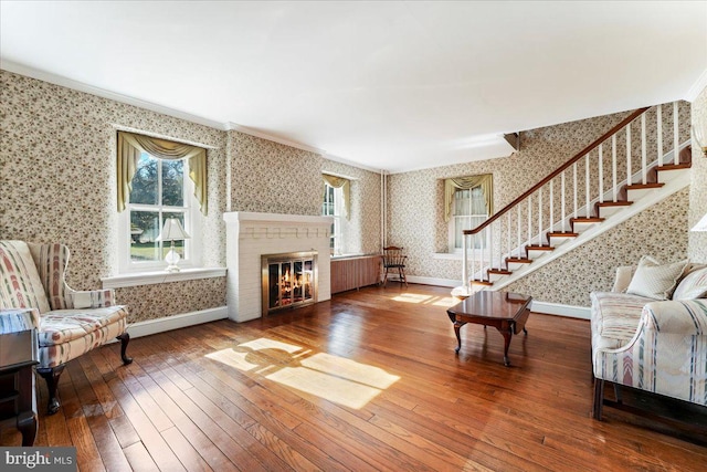 living room featuring a brick fireplace, radiator heating unit, wood-type flooring, and ornamental molding