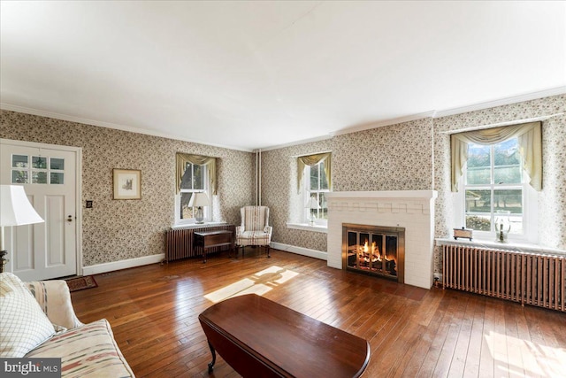 unfurnished living room featuring hardwood / wood-style floors, radiator, and a brick fireplace