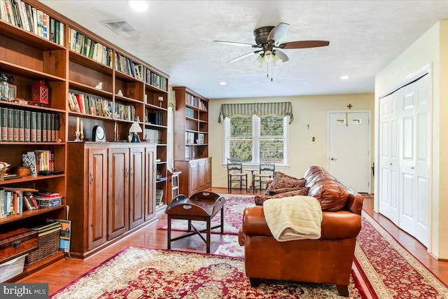 living area with ceiling fan, a textured ceiling, and light hardwood / wood-style flooring