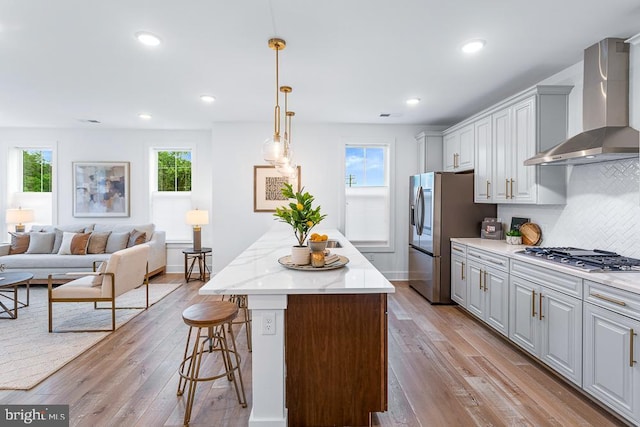 kitchen with wall chimney exhaust hood, light hardwood / wood-style flooring, a center island, stainless steel appliances, and tasteful backsplash