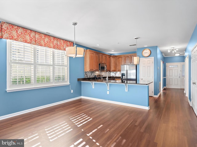 kitchen with pendant lighting, a breakfast bar area, decorative backsplash, kitchen peninsula, and stainless steel appliances