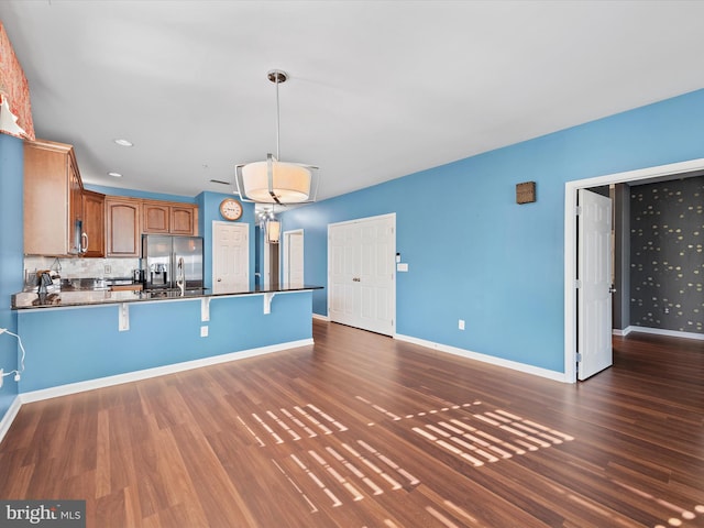 kitchen featuring pendant lighting, dark wood-type flooring, kitchen peninsula, tasteful backsplash, and stainless steel fridge with ice dispenser