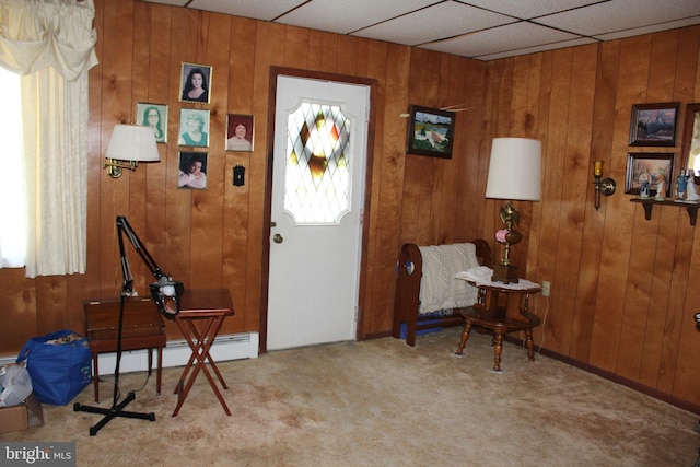 carpeted foyer entrance with a drop ceiling, wood walls, and baseboard heating