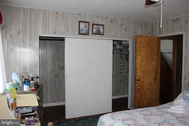 bedroom featuring a closet, dark carpet, ceiling fan, and wooden walls