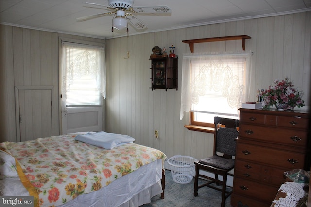 bedroom with ceiling fan, wooden walls, and ornamental molding