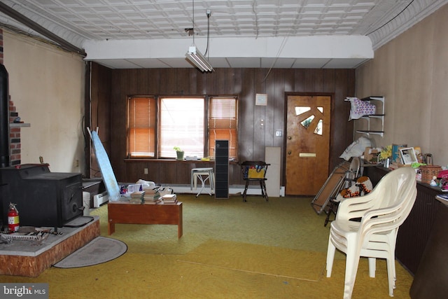 carpeted living room with wooden walls, a wood stove, and a baseboard heating unit