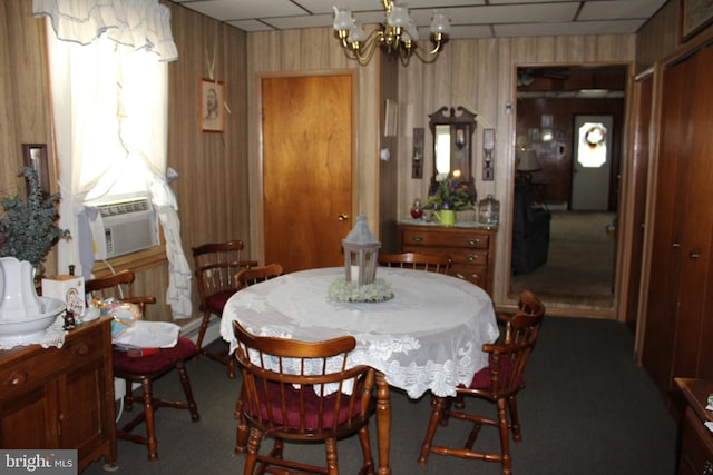 carpeted dining room featuring a paneled ceiling, cooling unit, wood walls, and a chandelier