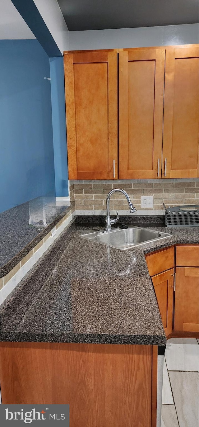 kitchen featuring decorative backsplash, dark stone counters, and sink