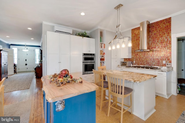 kitchen featuring wall chimney range hood, appliances with stainless steel finishes, hanging light fixtures, a center island, and white cabinets