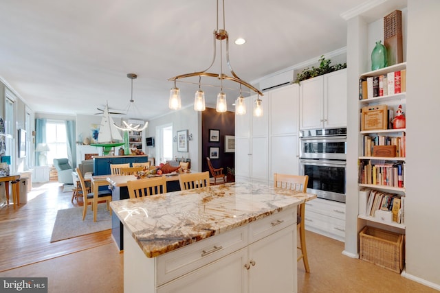 kitchen featuring ornamental molding, stainless steel double oven, a kitchen island, decorative light fixtures, and white cabinetry