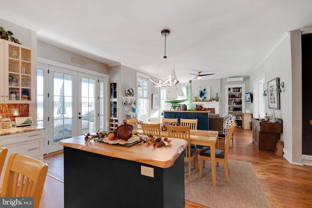 dining space with french doors, crown molding, an inviting chandelier, a wall mounted air conditioner, and light hardwood / wood-style flooring