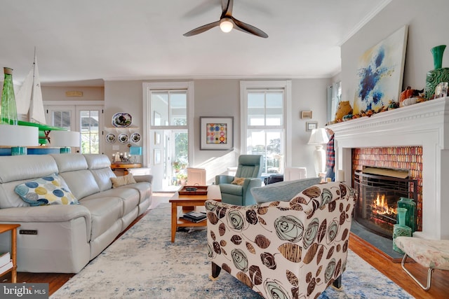 living room featuring a fireplace, ornamental molding, ceiling fan, and light wood-type flooring