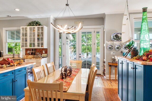 dining space featuring french doors, an inviting chandelier, sink, crown molding, and light hardwood / wood-style flooring